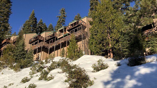 Un edificio de varios pisos con balcones exteriores, rodeado de nieve y árboles.