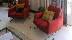 A living room with two red armchairs, a television, a painting, zebra-patterned curtains, and a radiator.