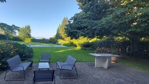 An outdoor patio with a pool, surrounded by lush greenery and trees.