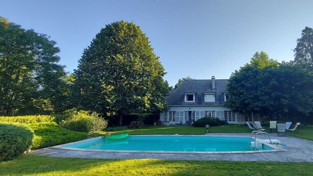 A house with a swimming pool, surrounded by a well-maintained lawn and trees.