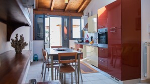 Een moderne keuken met rode kastjes, een eettafel met stoelen en uitzicht naar buiten.