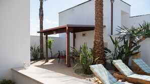 Een terras met twee lounge fauteuils, een houten pergola en een kleine tafel met stoelen.