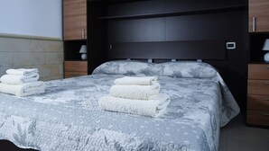 Een net opgemaakt bed met een gebedrukte spreidek en twee opgevouwen handdoeken aan de zijkant.