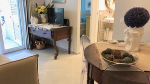 A dining area with a wooden table, chairs, and a vase with flowers. There is a television on a stand and a window with blinds. - Casa Mando Terrace With Private Jacuzzi - Taormina (Taormina)
