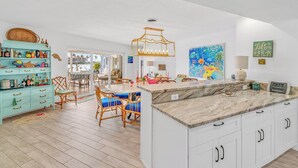 A spacious kitchen with a marble countertop, wooden chairs, and a dining table.
