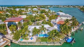 An aerial view of a coastal property with a swimming pool, multiple buildings, and a dock.