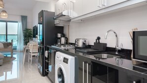 A modern kitchen with a built-in washer and dryer, a large island with a sink, and a dining area with a view of the city. - HiGuests - Elite Business Bay (Dubai)