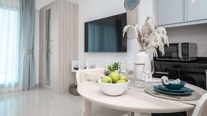 A modern dining area with a white table, a bowl of fruit, and a vase of dried plants. - HiGuests - Elite Business Bay (Dubai)