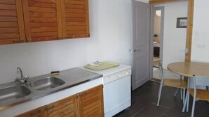 A compact kitchen with wooden cabinets, a sink, a dishwasher, and a small dining table with chairs.