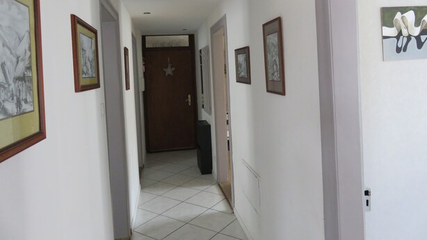 A hallway with framed pictures on the walls, a door at the end, and a tiled floor.