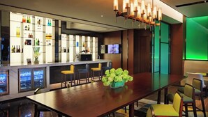 Un área de bar moderna con una larga mesa de madera, varios taburetes y una variedad de botellas en estantes.