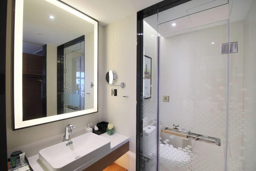 A modern bathroom with a large mirror, a white sink, and a glass shower enclosure.