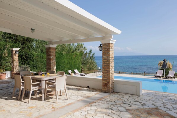 A covered outdoor area with a pool, lounge chairs, and a dining table.
