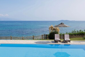 A pool with two lounge chairs and an umbrella, overlooking a body of water.