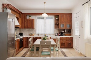 A kitchen with wooden cabinets, a stainless steel refrigerator, a dining table with chairs, and a pendant light.