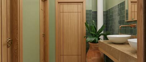 A bathroom with a wooden door, a large mirror, a sink, and two terracotta pots.