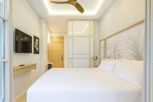 A modern bedroom with a large bed, a ceiling fan, a TV, and artwork on the walls.