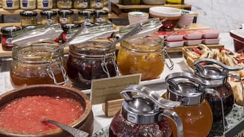 Diversos alimentos, incluyendo frascos de conservas, un cuenco de madera con compota de frutas, y un cartel que indica sabores como naranja, fresa y melocotón.