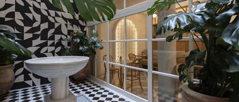 A bathroom with a checkered floor, a sink, and large windows with a view of a dining area.