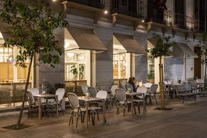 An outdoor cafe with tables and chairs, a tree, and a building with large windows and balconies. - Malabar by Petit Palace (Málaga)