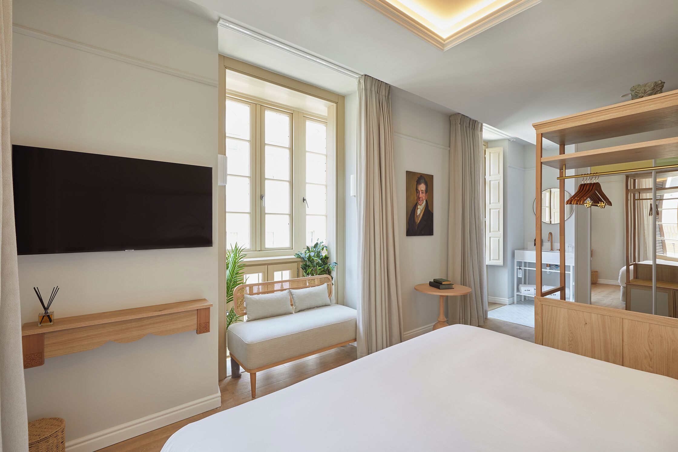 Een hotelkamer met een groot bed, een bank, een tv die aan de muur is bevestigd, een tafeltje en een spiegel.