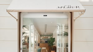 A hotel entrance with a white awning, a reception desk, and a view into the interior featuring a kitchen and seating area. - ICON Malabar (Málaga)