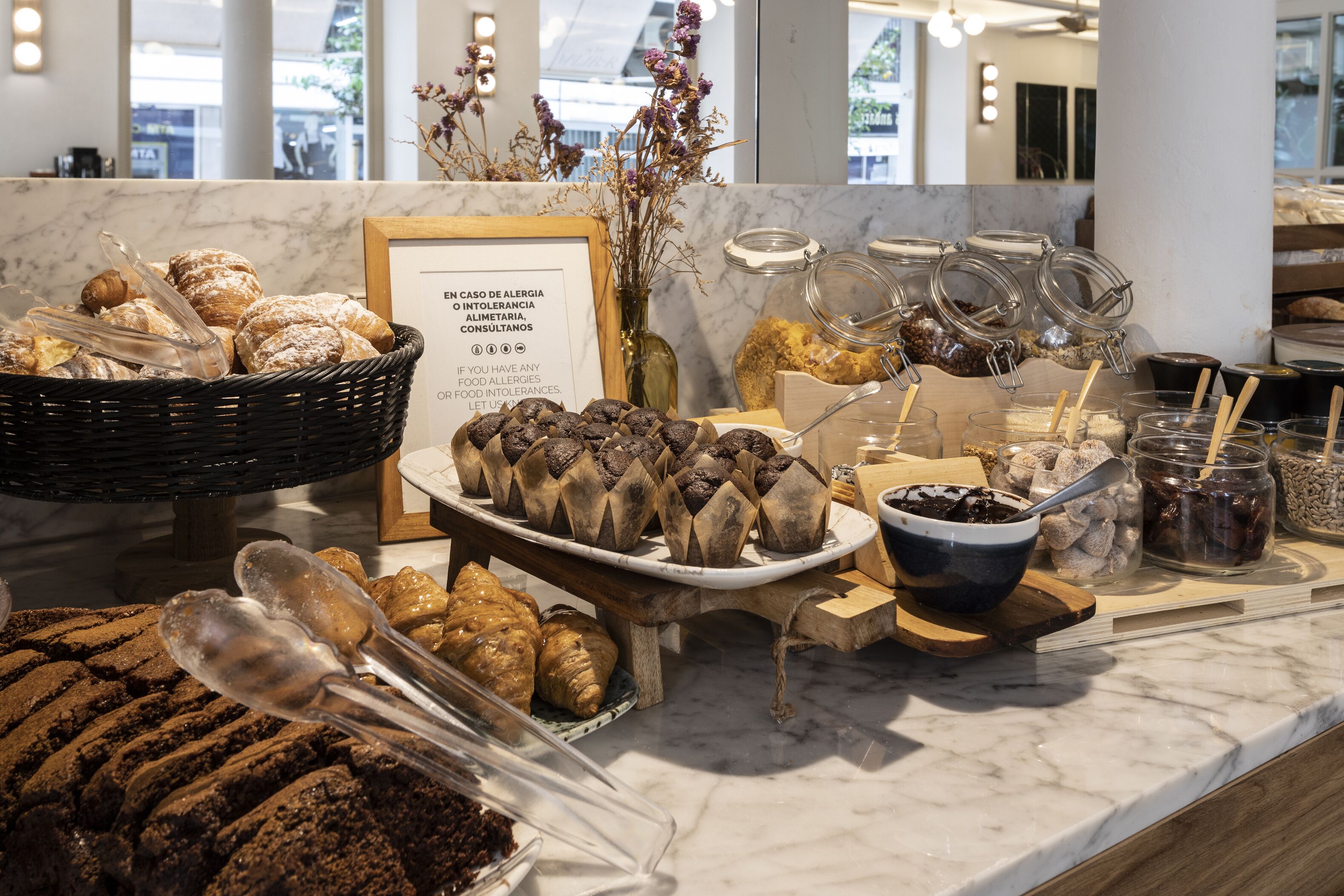 Eine Bäckertheke mit Gebäck, ein Schild zu Lebensmittelallergien und verschiedene Gläser mit Zutaten.