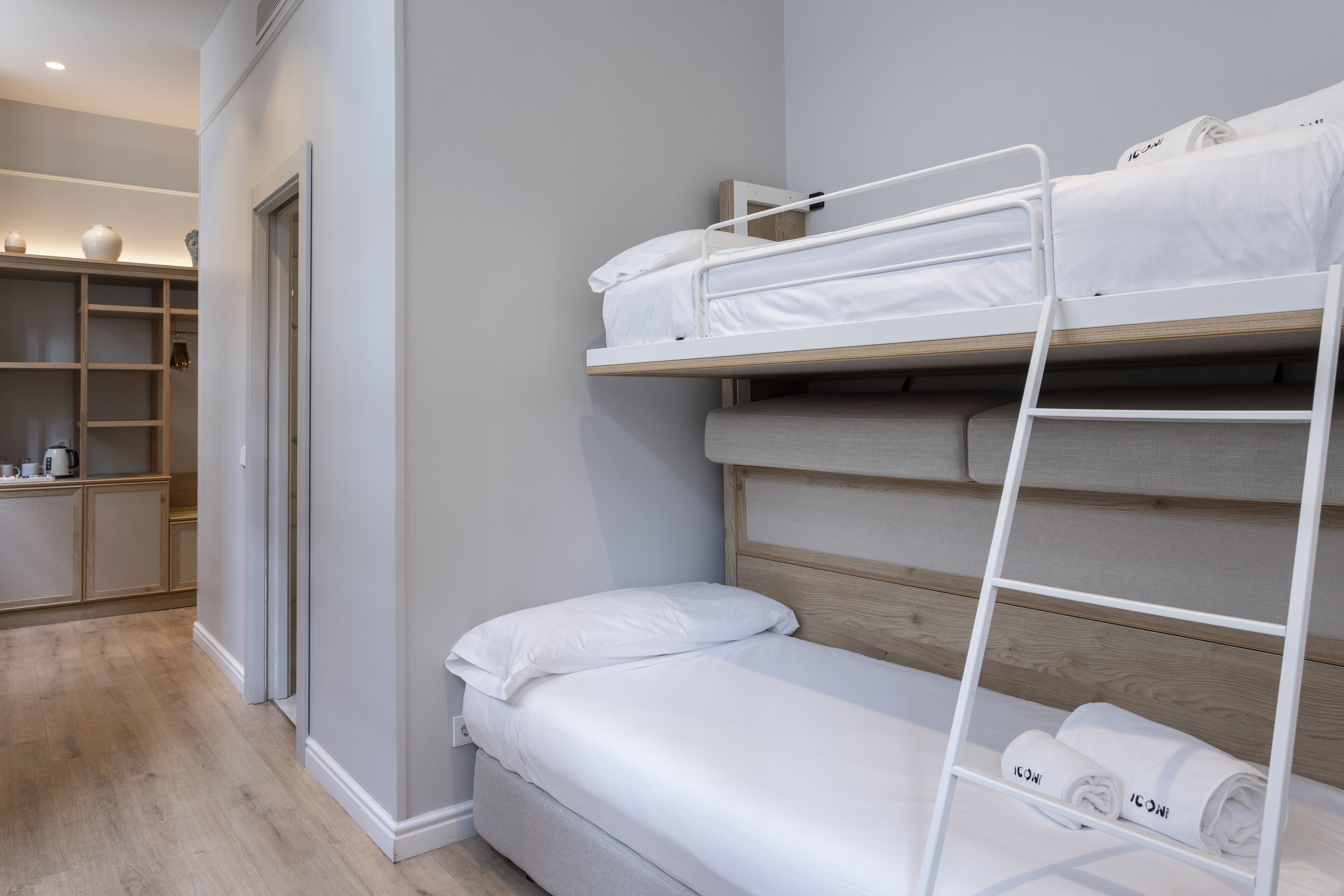 A bunk bed with white bedding and a wooden headboard, a wooden floor, and a built-in shelving unit with storage.
