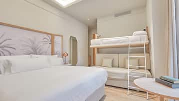 A hotel room with a large bed, a bunk bed, a small table, and a wall with a plant mural.