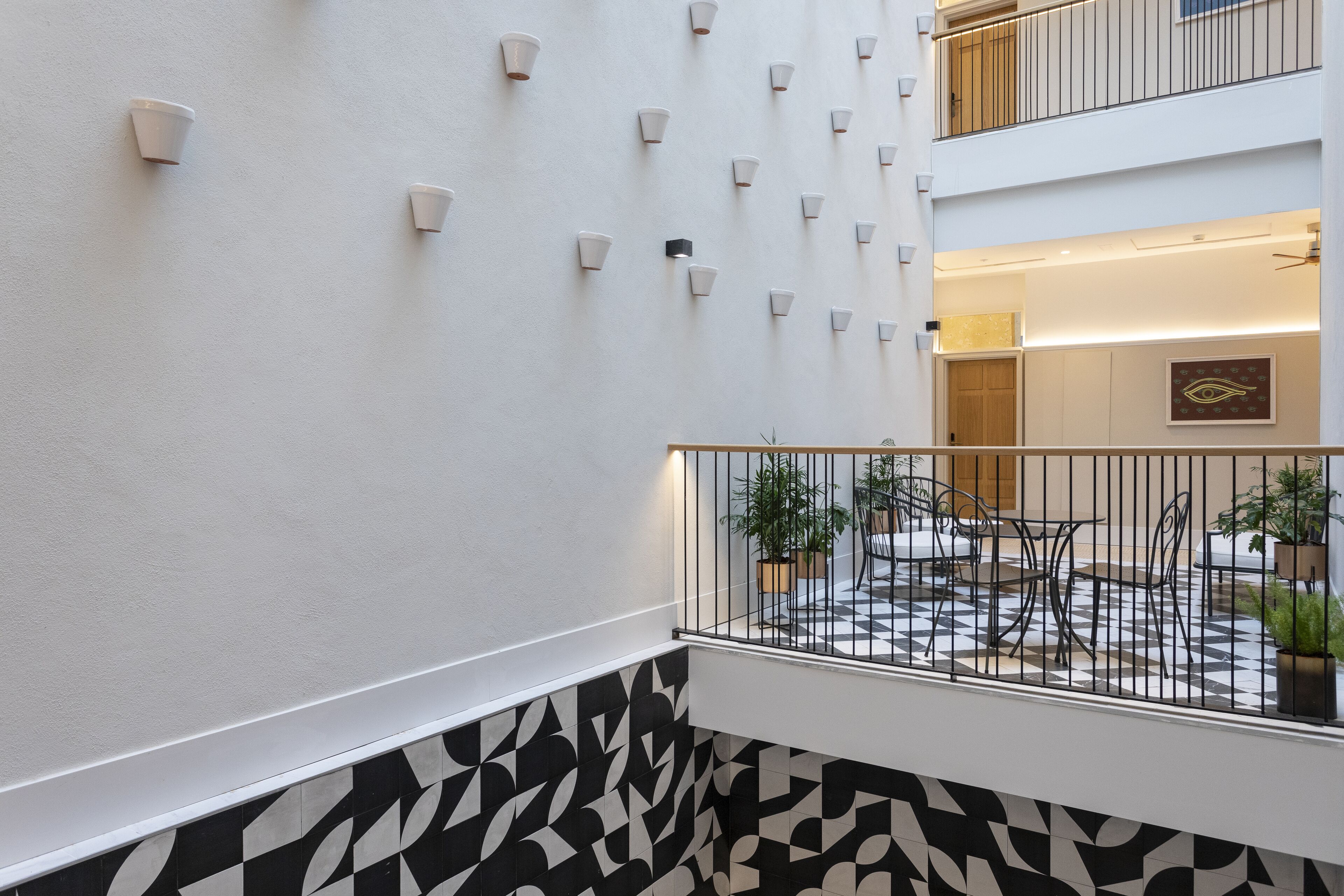 A modern interior with a patterned floor, a white wall with wall-mounted lights, and a balcony with outdoor seating.