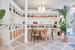 A modern library with white shelving, a round wooden table, and comfortable chairs.