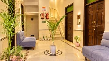 Un vestíbulo de hotel con piso de mármol, dos sofás, plantas en macetas, una escalera y un extintor.