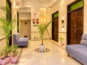 Un hall d’hôtel avec un sol en marbre, deux canapés, des plantes en pot, un escalier et un extincteur.