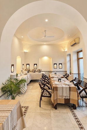 Une salle à manger spacieuse avec de hauts plafonds, un lustre central et un ventilateur de plafond.
