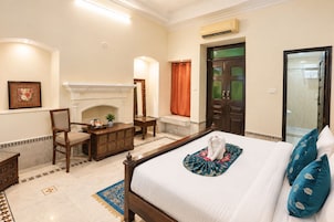 Habitación de hotel con cama, escritorio, silla, chimenea y baño visible a través de una puerta abierta.