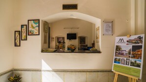 Uma área de recepção com obras de arte emolduradas, balcão de atendimento, televisão e um mural de avisos.