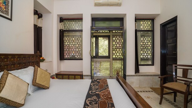 Quarto com cama grande, cabeceira de madeira, uma cadeira e janela com cortinas decorativas.
