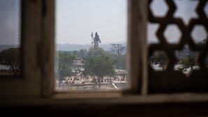 Vista pela janela com um painel decorativo, mostrando uma estátua ao longe e um parque com árvores e caminhos.