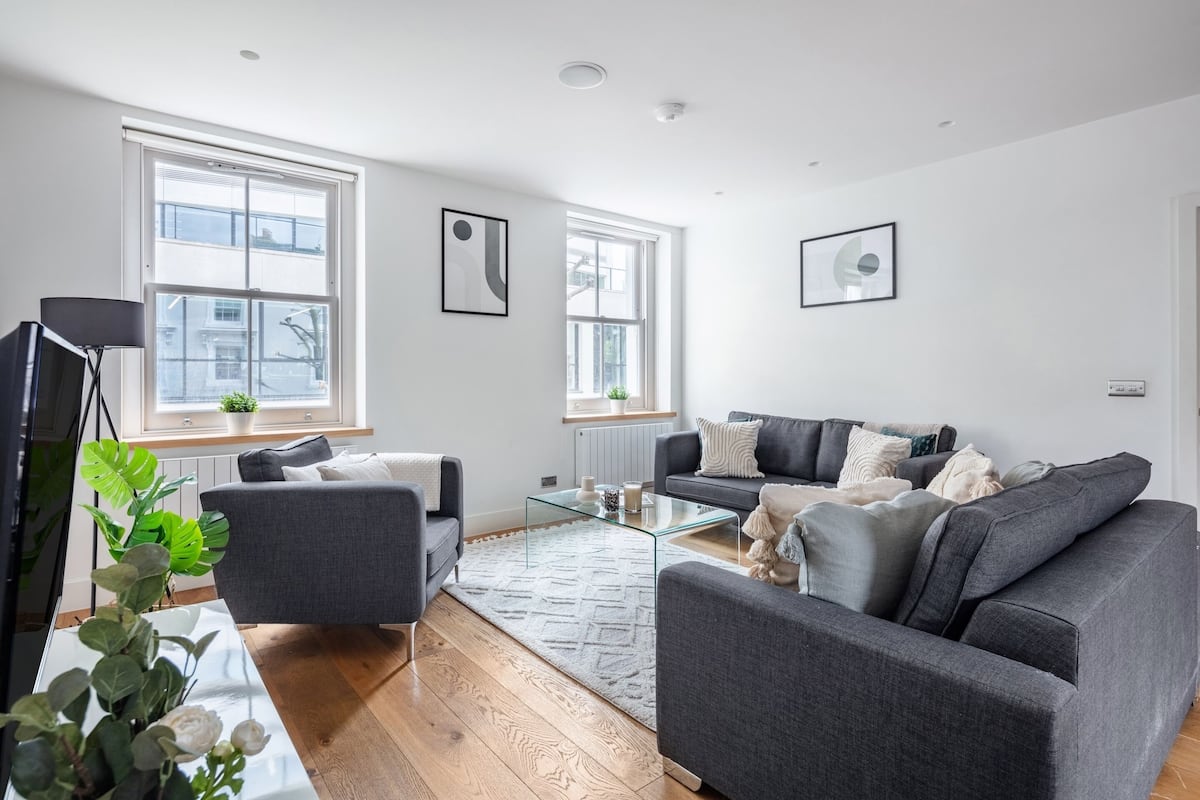 Una sala de estar moderna con un sofá gris, una mesa de centro de vidrio y un televisor sobre un mueble.