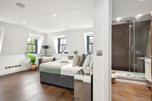 Relax in this serene bedroom with a large bed, flanked by two windows and a glass shower enclosure.