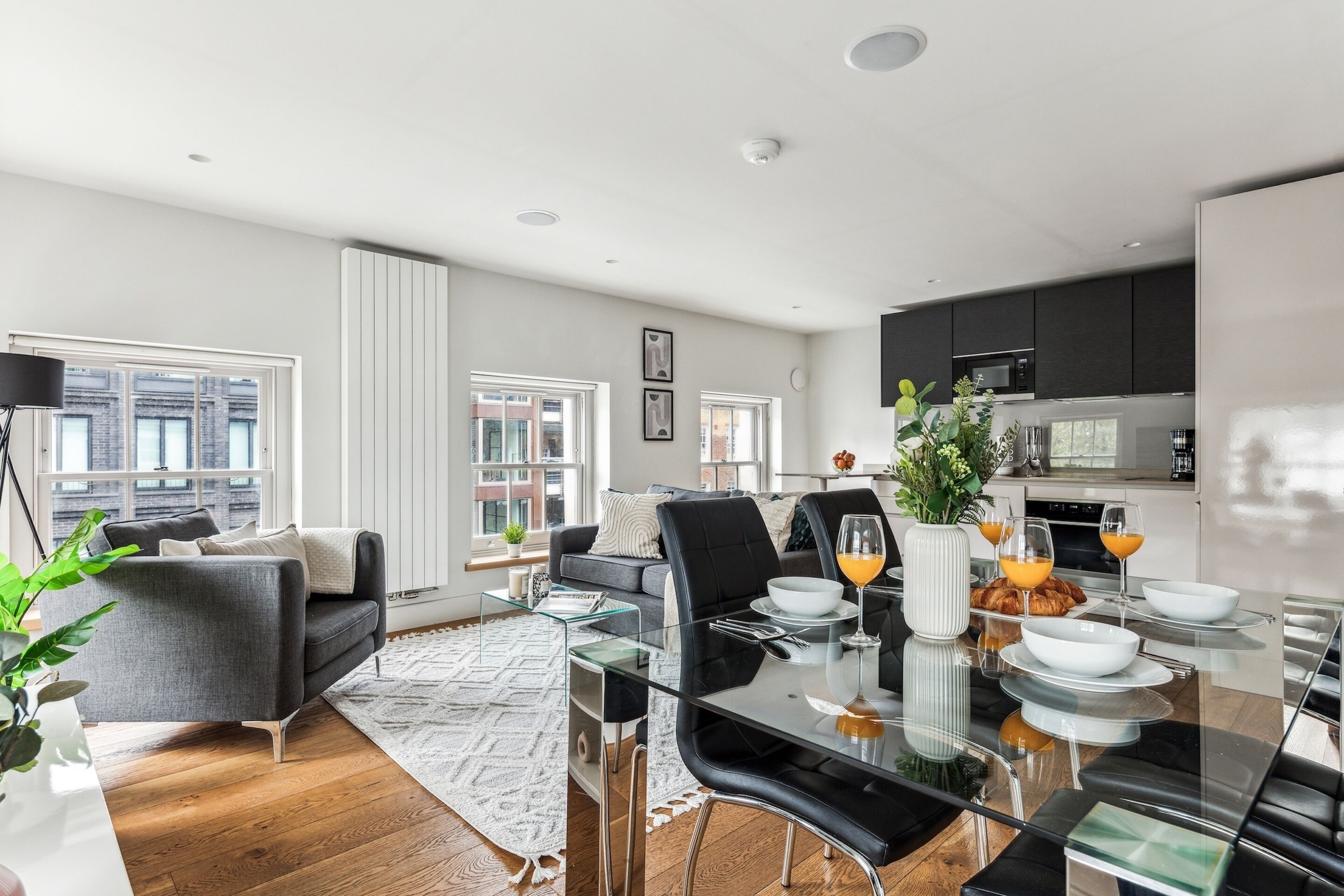 Una sala de estar moderna con una mesa de comedor de vidrio, sillas de cuero negro y un sofá gris.