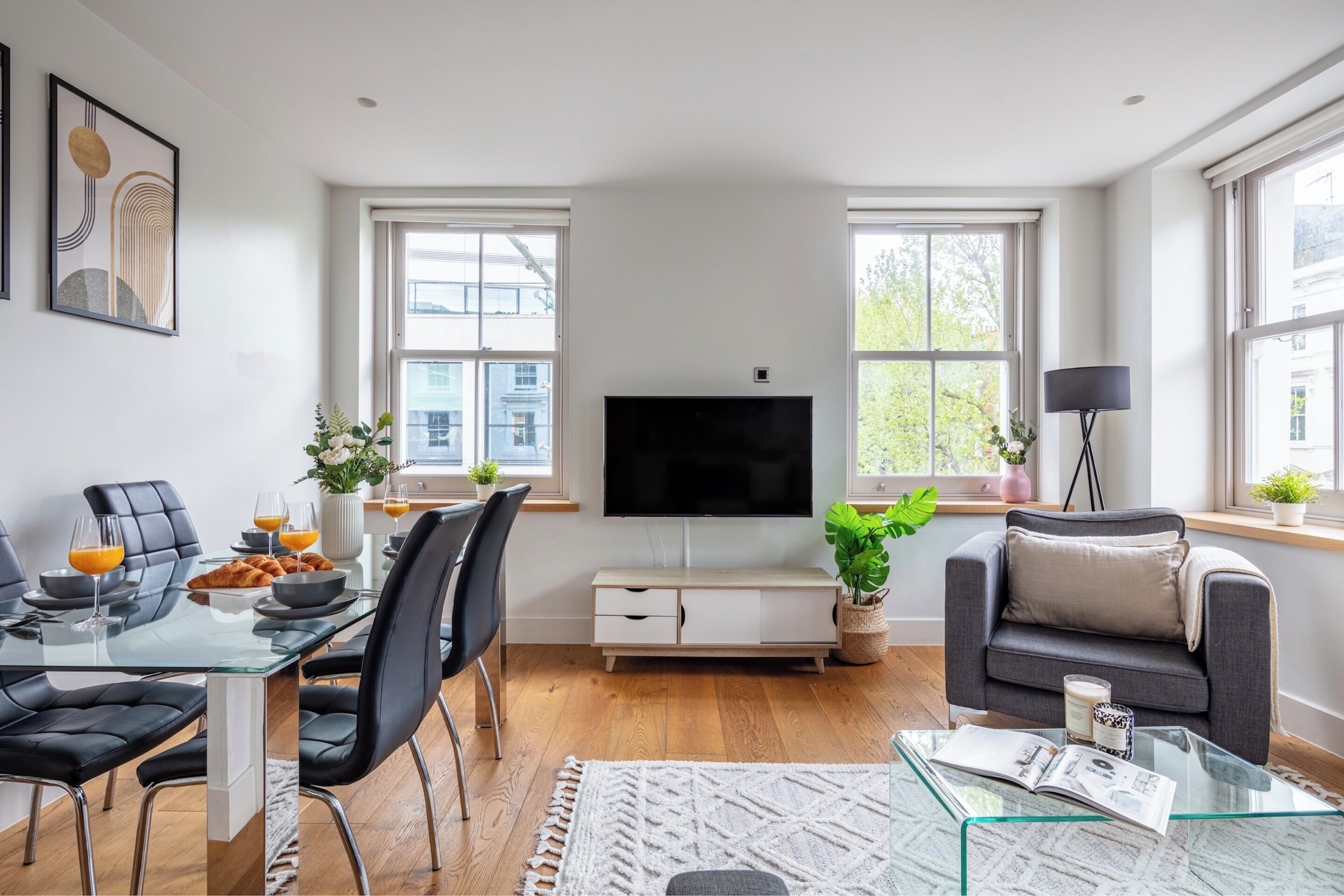 Un salon moderne avec une table à manger en verre, des chaises noires, un téléviseur à écran plat, un canapé gris et une table basse.