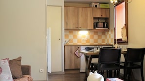 Un espace de vie compact comprenant un coin cuisine, un espace repas avec une table et des chaises, et un canapé agrémenté de coussins décoratifs.