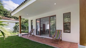 Una casa moderna con un patio, dos sillas de playa a rayas y un cerramiento de vidrio corredizo que da a un espacio interior.