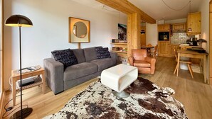 A modern living room with a sofa, a white ottoman, a cowhide rug, a floor lamp, and a dining area with wooden furniture.