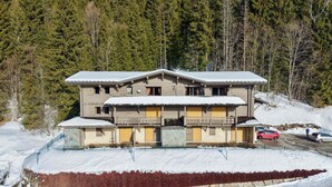 A multi-story building with a snow-covered roof, surrounded by trees.