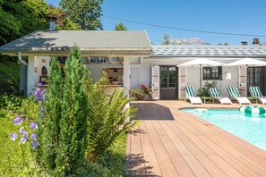 Uma casa com deck de madeira, piscina e jardim com diversas plantas e flores.