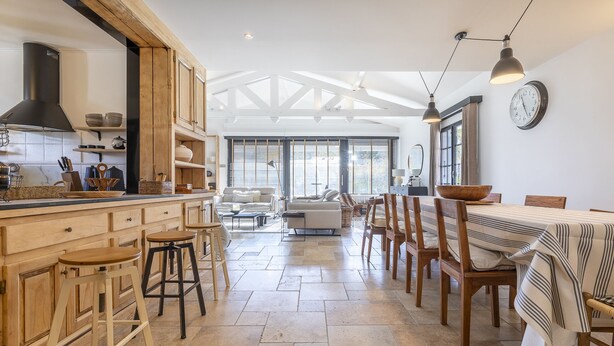 Una cocina amplia con armarios de madera, un comedor con mantel a rayas y un ventanal que proporciona luz natural.