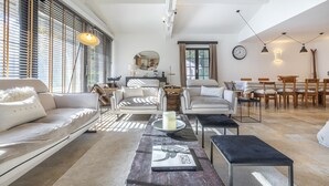 Un salón amplio con sofá, sillones, una mesa de centro y una zona de comedor con mesa y sillas.