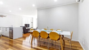 Eine moderne Küche mit Geschirrspüler, ein Essbereich mit weißem Tisch und gelben Stühlen sowie ein graues Sofa im Hintergrund.